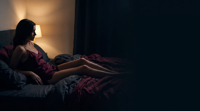 A woman reclining on dark bedding in warm lamplight